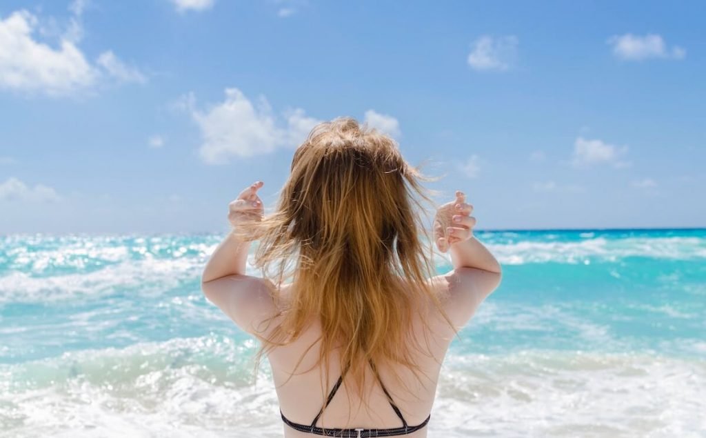 moteris, stovinti paplūdimyje, žvelgianti į jūrą, kad gautų saulės poveikio